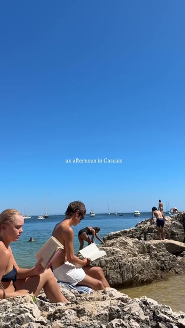 Travelers reading on the rocks beside the water in Cascais